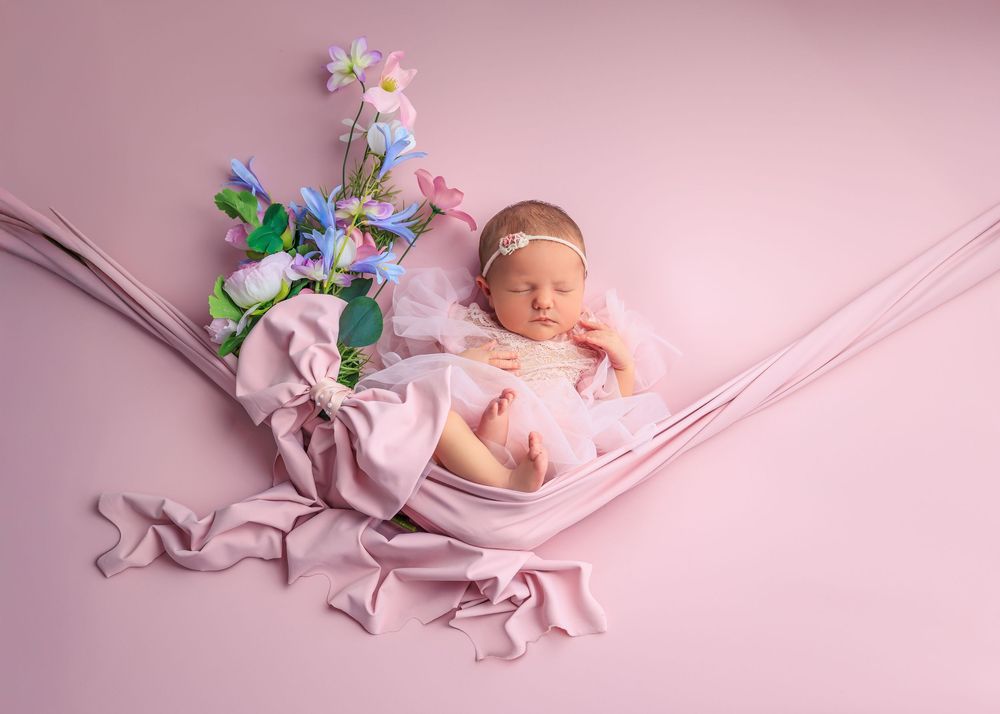 Sleeping newborn wrapped in soft pink fabric with delicate flowers on a pink background.