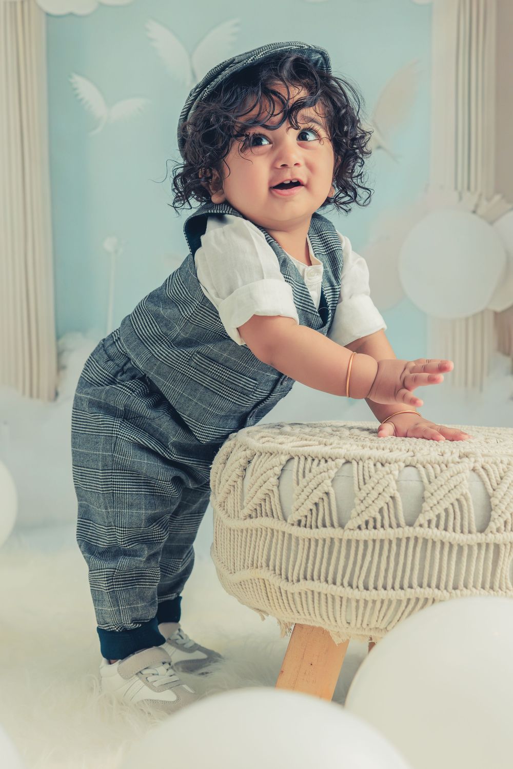 Toddler in grey outfit playing on macrame swing against dreamy cloud backdrop.