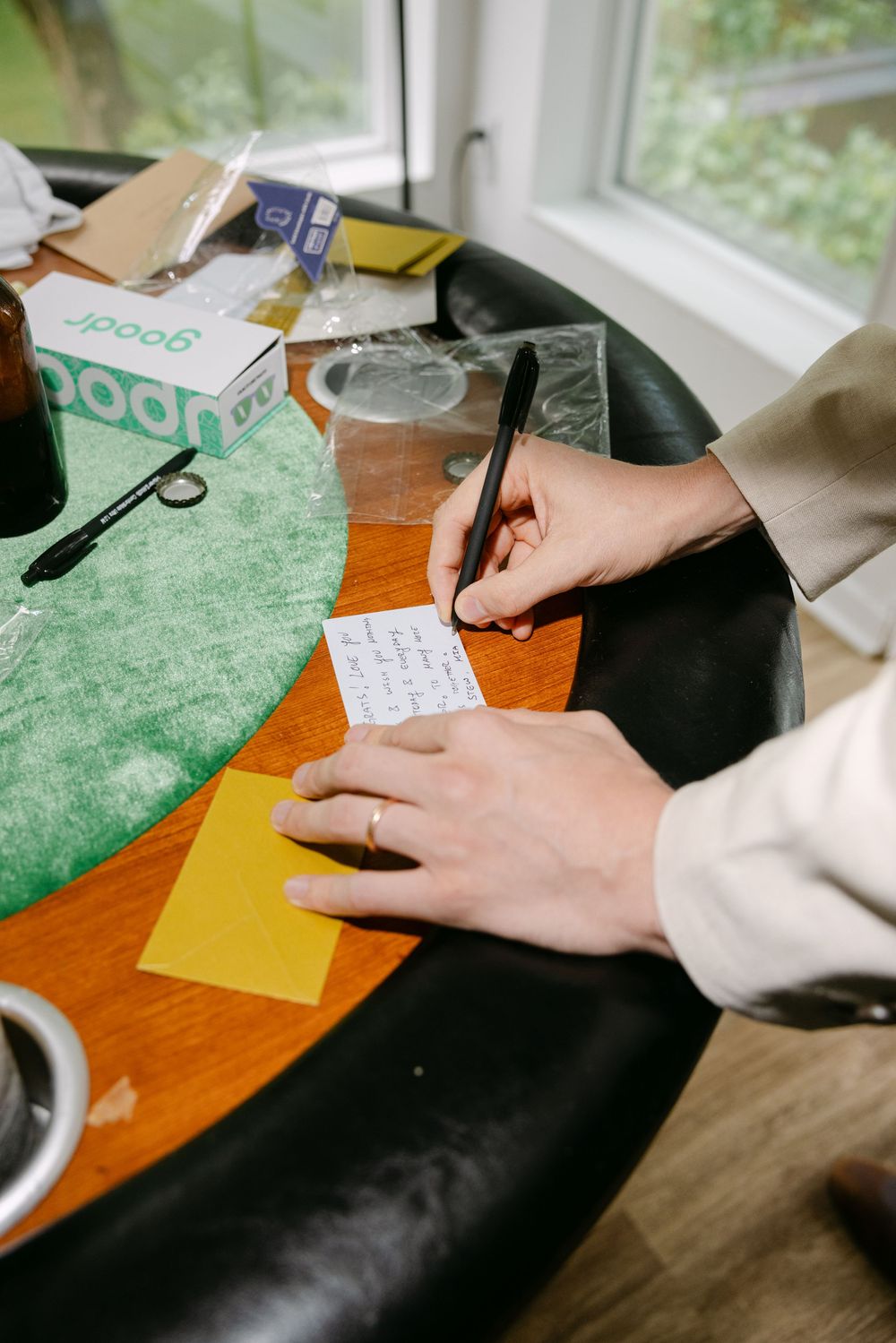 Close-up view of hands writing and working with paper on a wooden desk near a bright window.