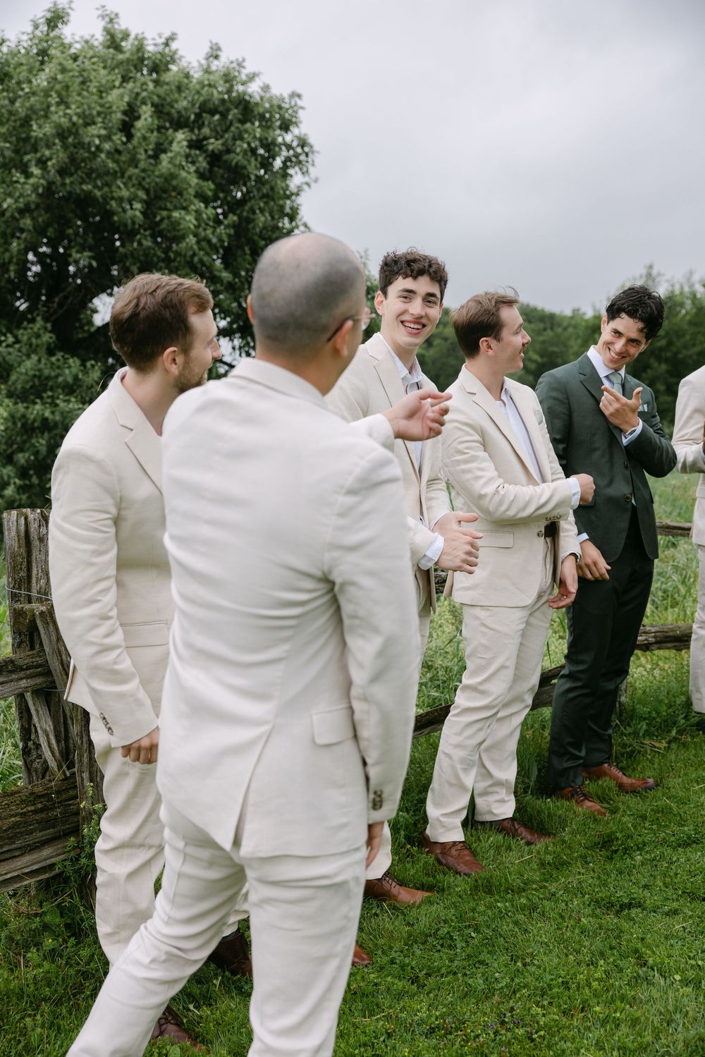 A group in white suits lined up outdoors showing playful domino-like falling poses on grass.