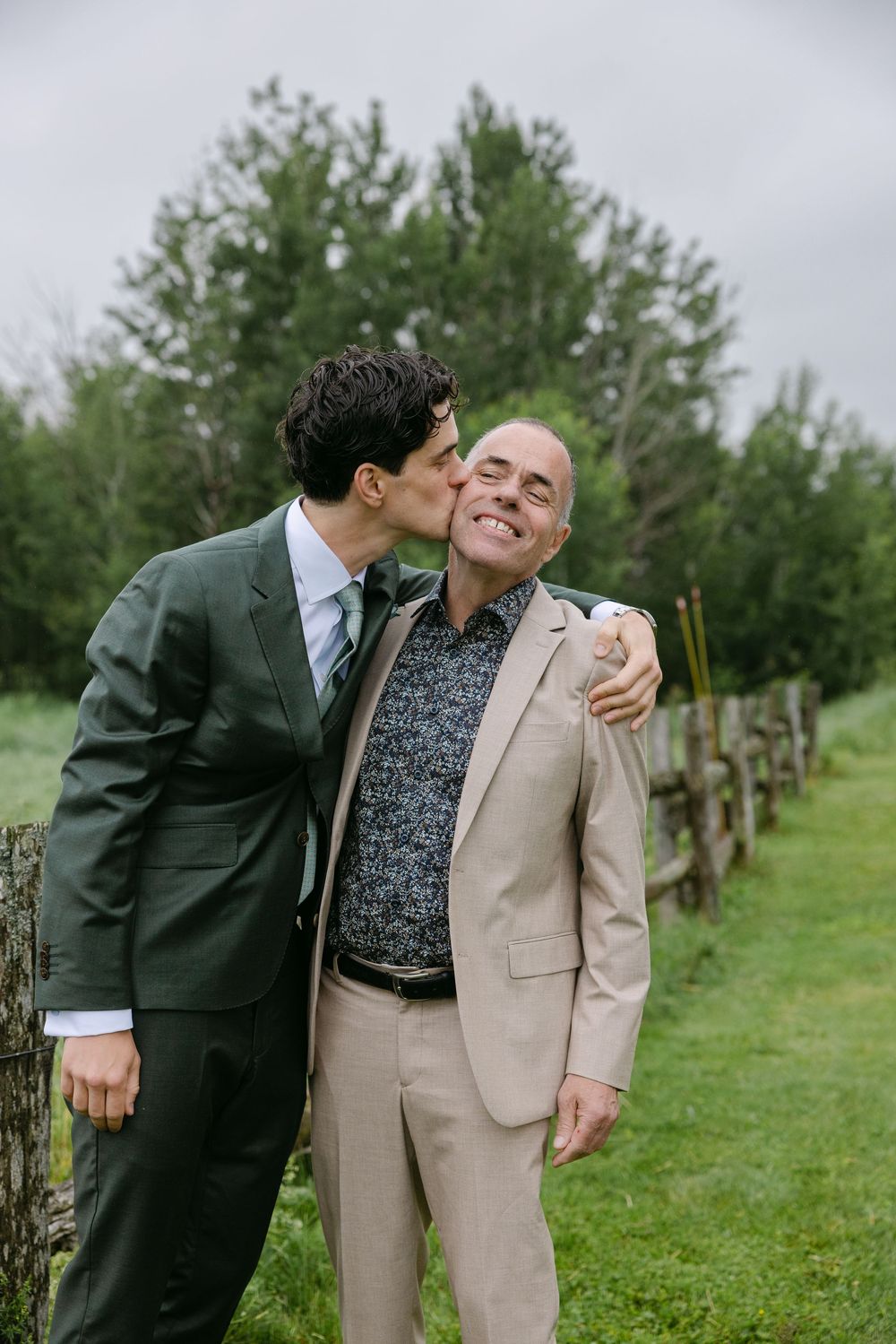 Two people in a romantic moment share playful kisses while standing together in an orchard on a green summer day.