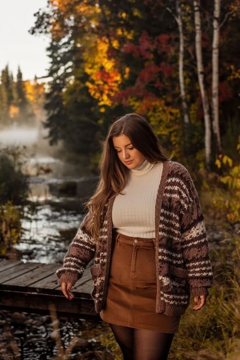 A couple in autumn attire poses together on fallen leaves against a rustic stone wall backdrop.
