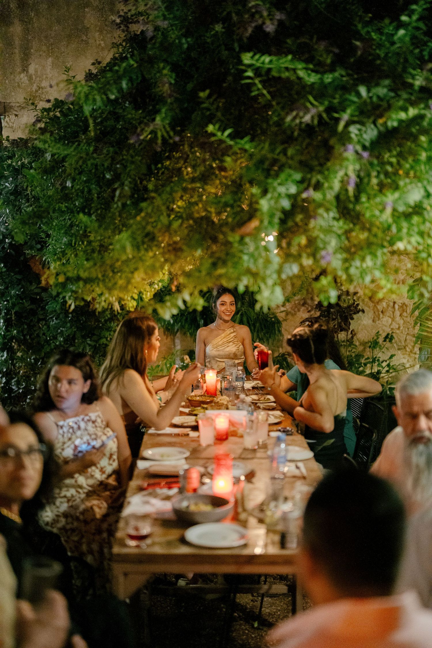A candlelit outdoor dinner gathering with people seated at a long table under trees creating an intimate ambiance.