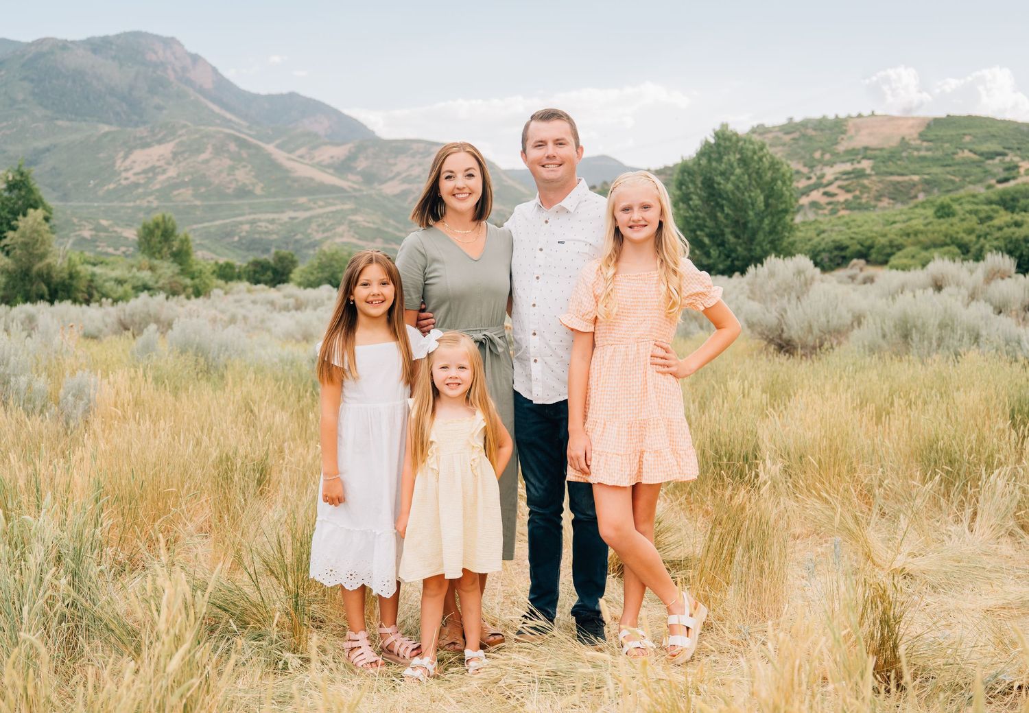 A group stands together outdoors in a field with mountains and sagebrush in the background.