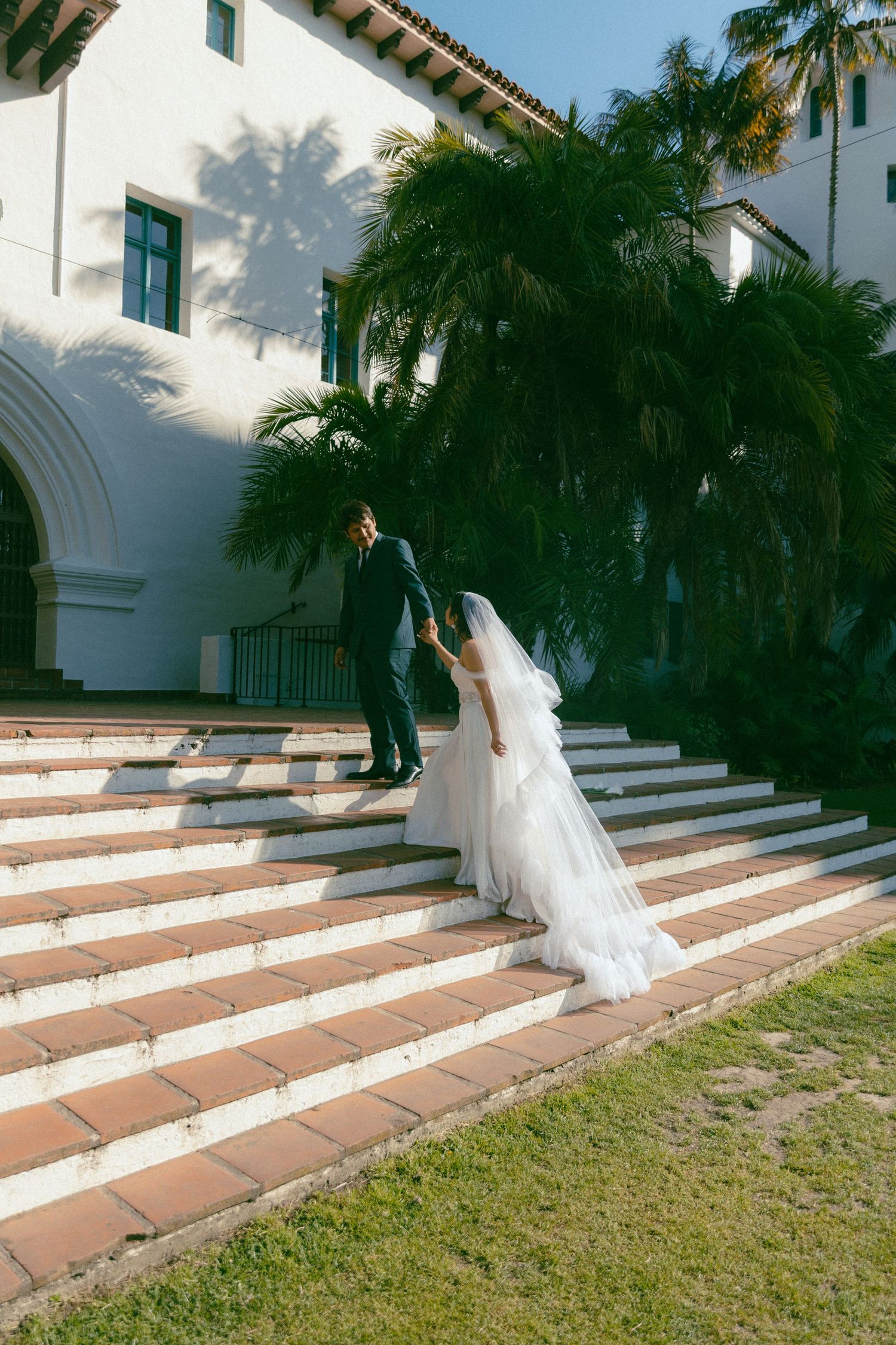A romantic wedding moment captured through a flowing white veil against a Mediterranean style building backdrop.