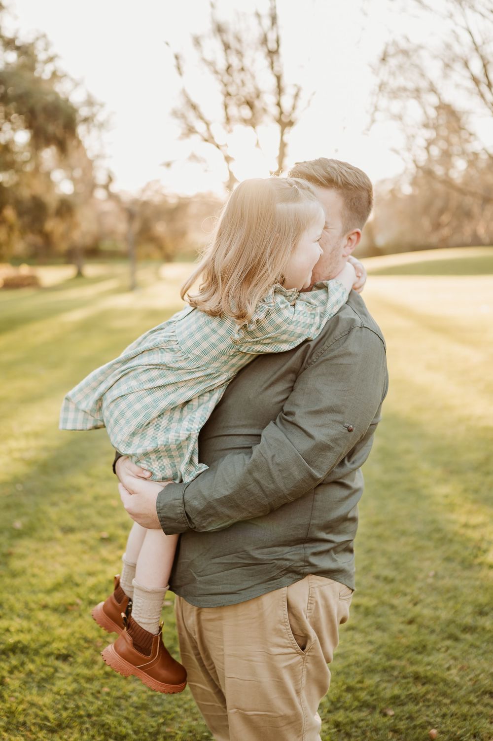 Sweet candid moment between parent and child during golden hour in a grassy park.
