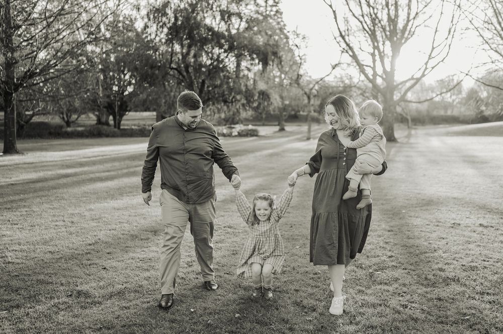 A family walks hand-in-hand along a tree-lined path in a black and white vintage photograph.