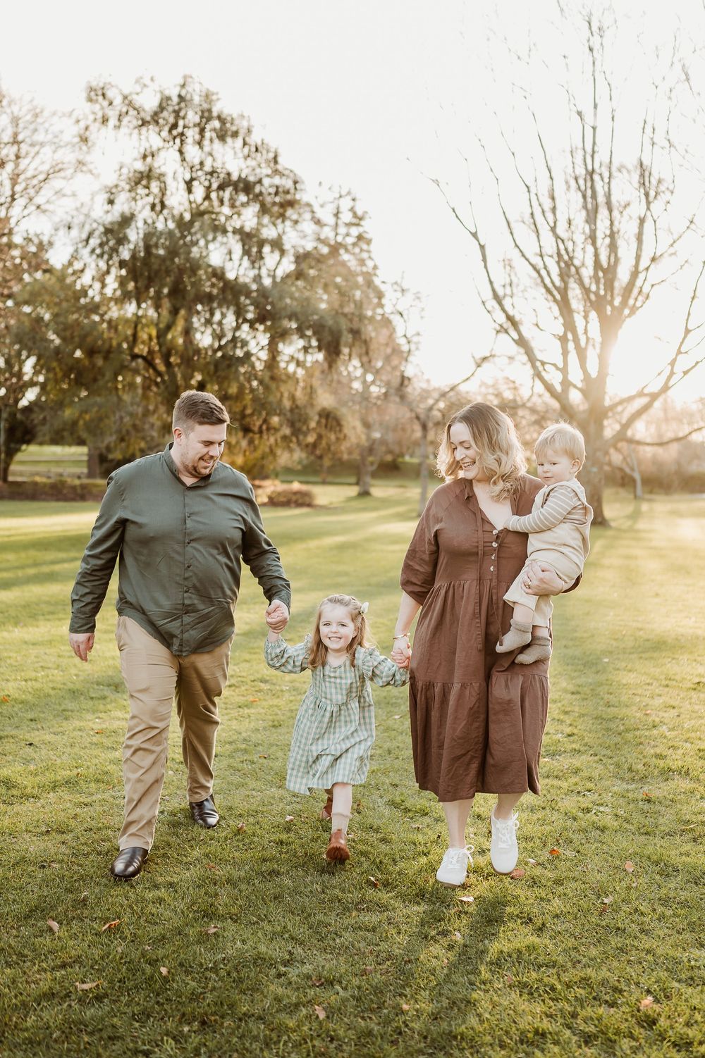 A family walking together on a sunlit grassy field during golden hour.