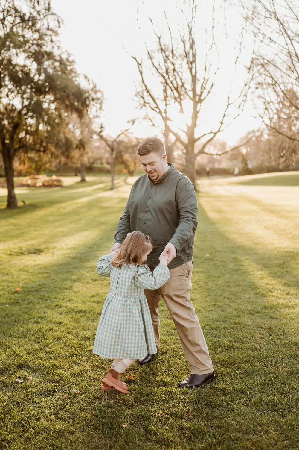 A heartwarming sunset photo of family members dancing together on a lush green lawn in autumn.