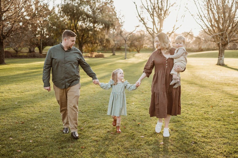 Family walking together across a sunlit grassy field on an autumn evening.