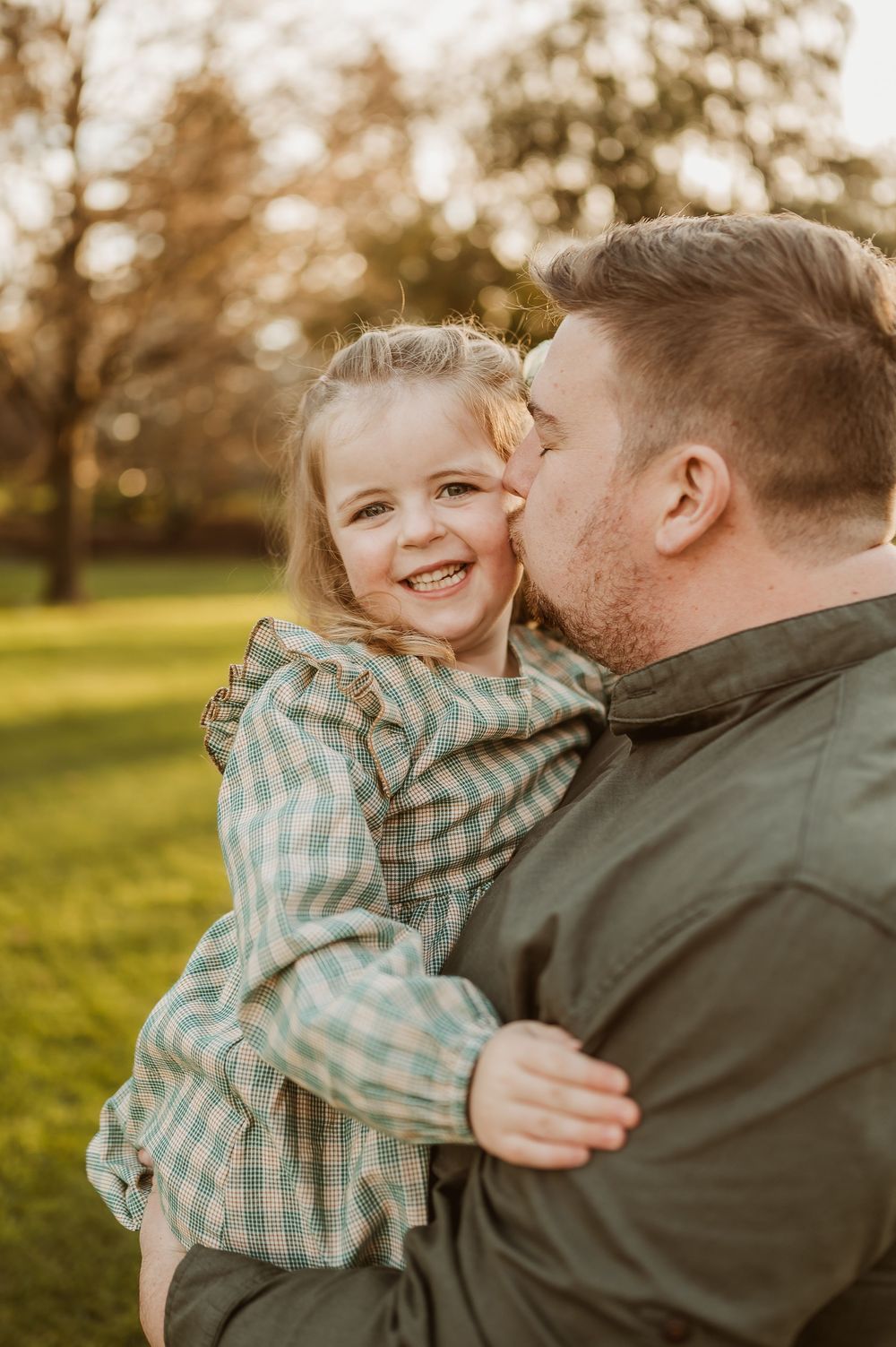 A tender moment captured between parent and child laughing together in a sunlit park setting.