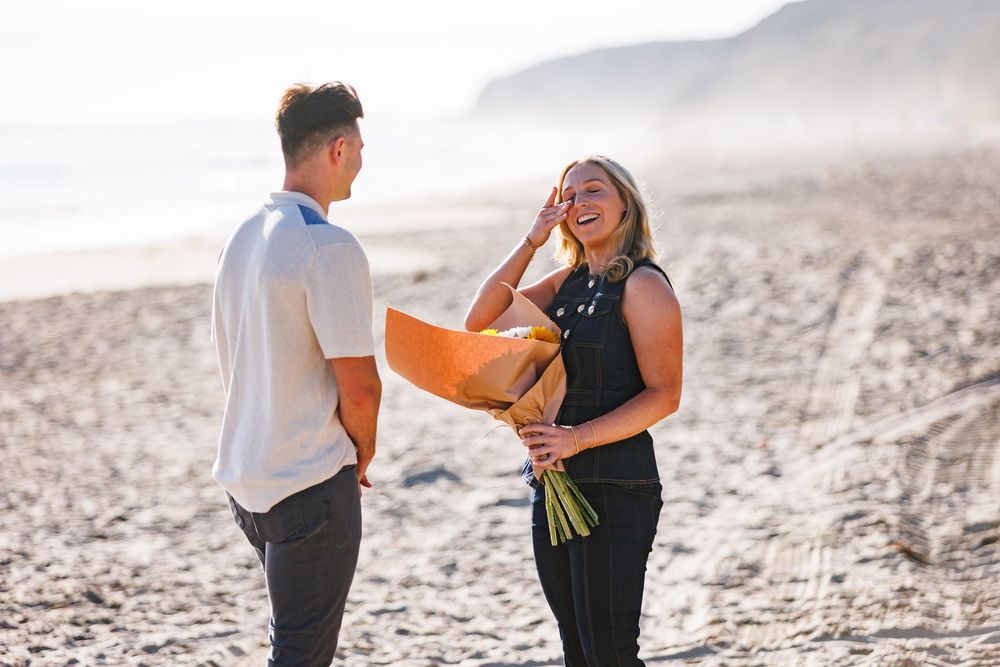 A couple joyfully embraces on a scenic beach at sunset during a romantic proposal moment.