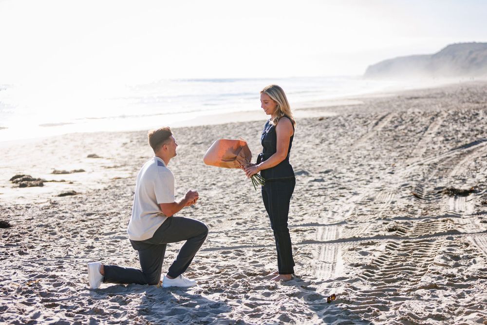A couple sharing a romantic propsal on a misty beach during sunset in Newport Beach in Crystal Cove.