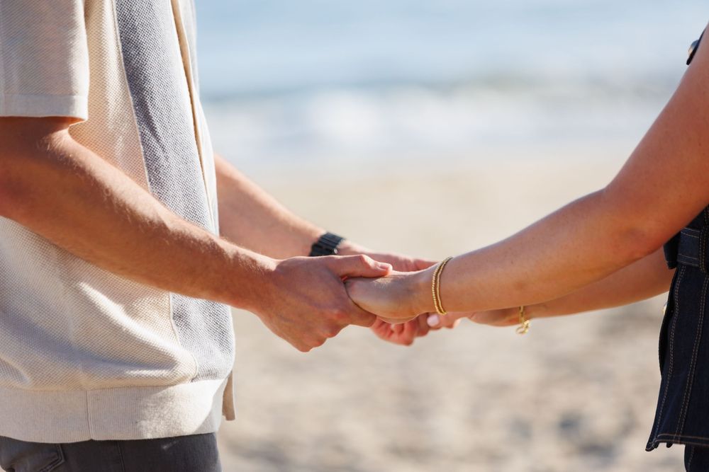 Close-up shot of hands holding heart-shaped rings during a symbolic beach wedding ceremony.