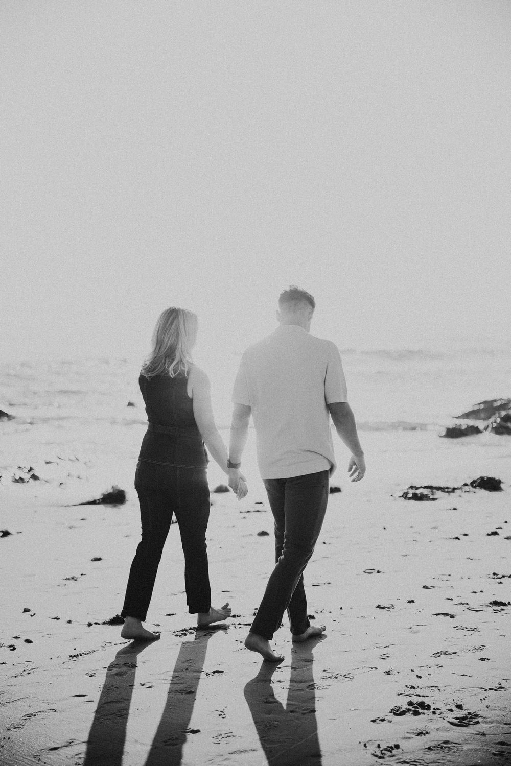 Black and white photo series of two people walking together on a beach creating long shadows on the sand.