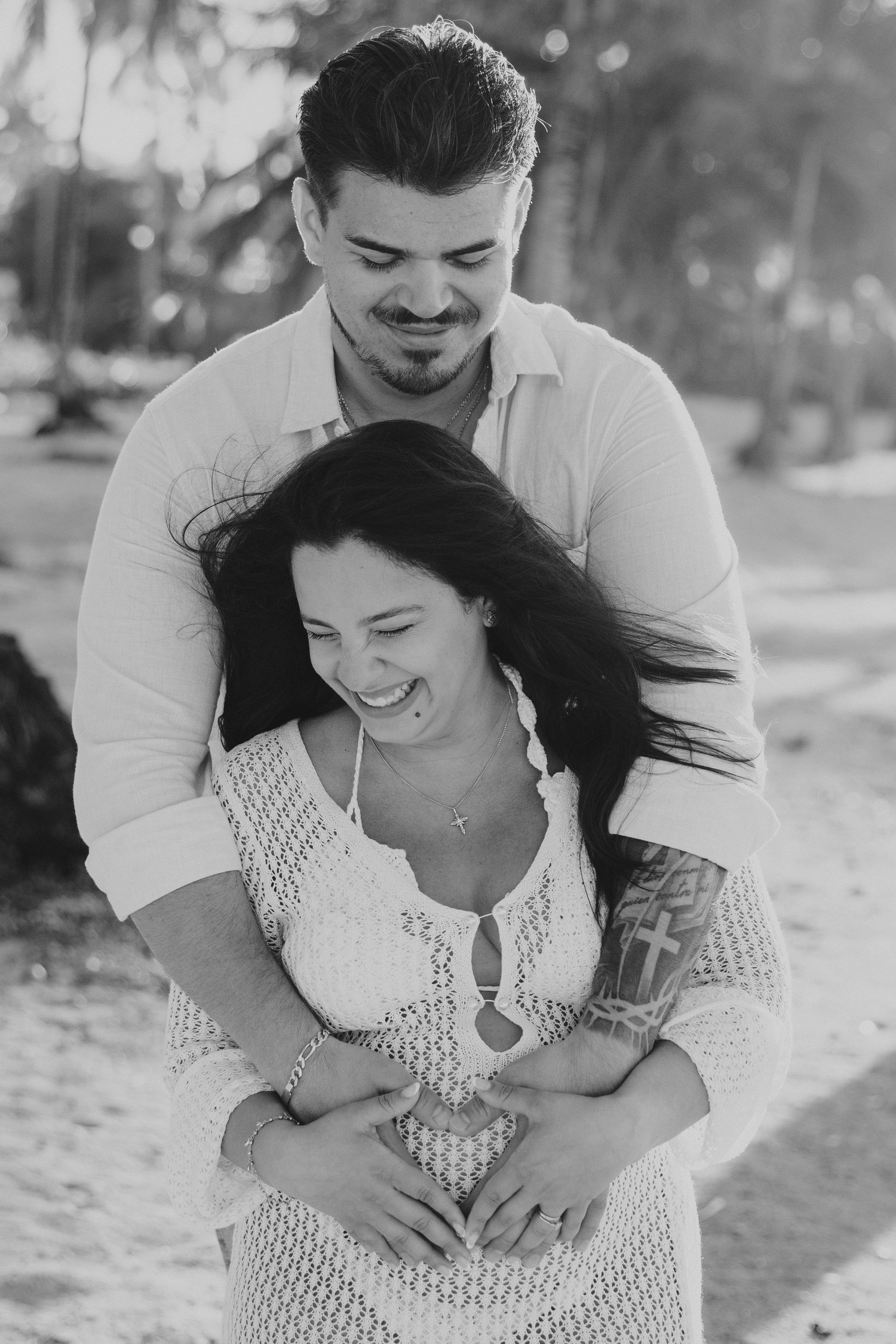 A black and white portrait of a couple laughing and embracing on a tropical beach.