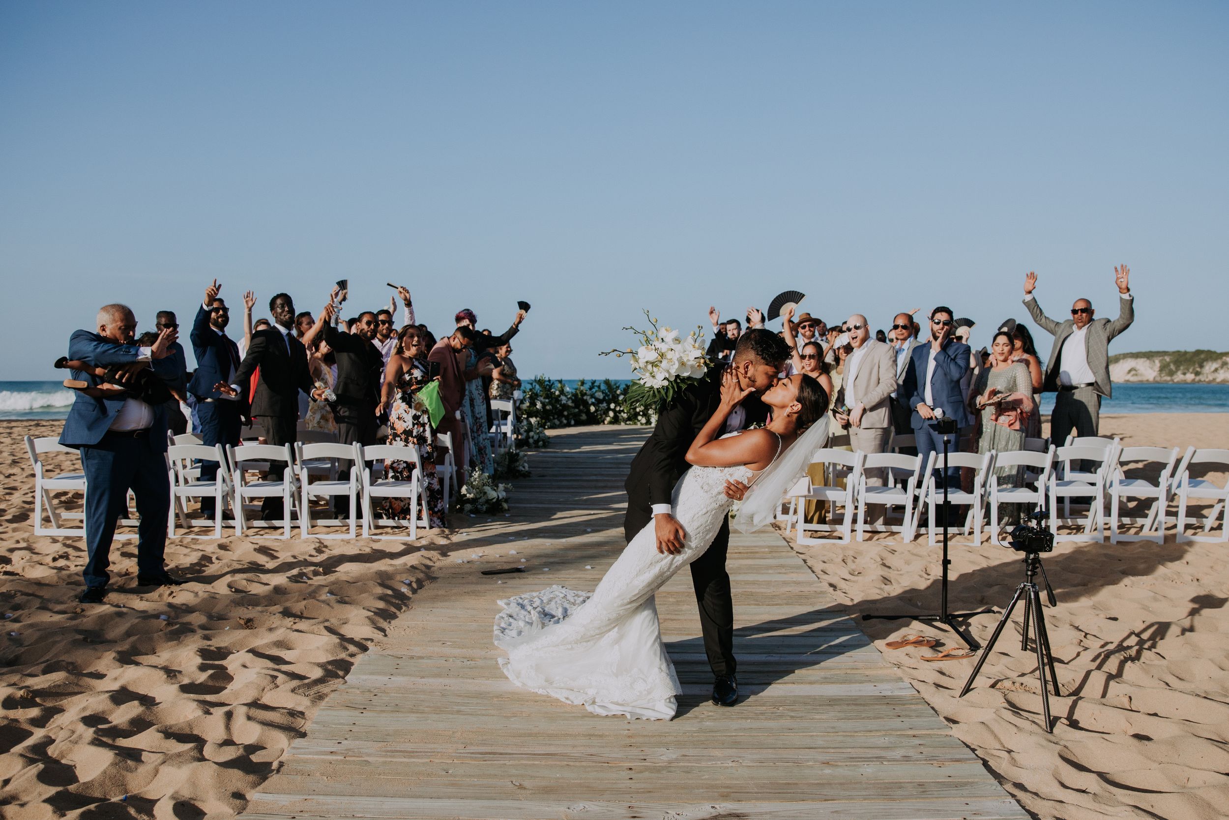 Wedding guests celebrating on a sandy beach boardwalk.