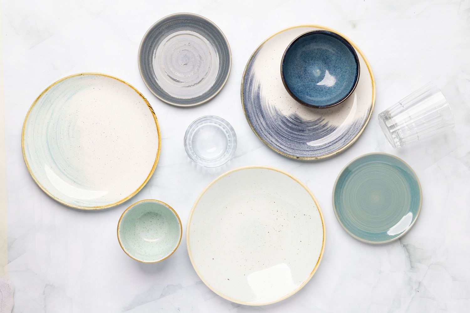 Collection of modern ceramic plates and bowls in soft blue and white tones with gold trim.