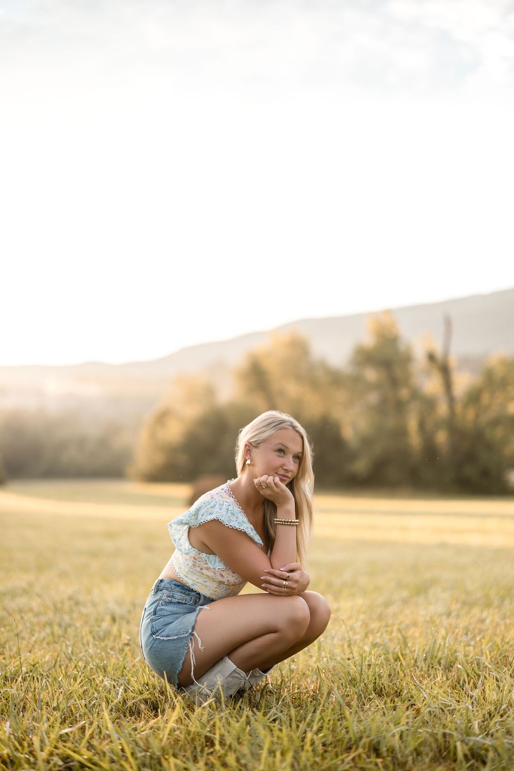 A casual summer portrait in a sunlit meadow with mountains and trees in the golden hour light.