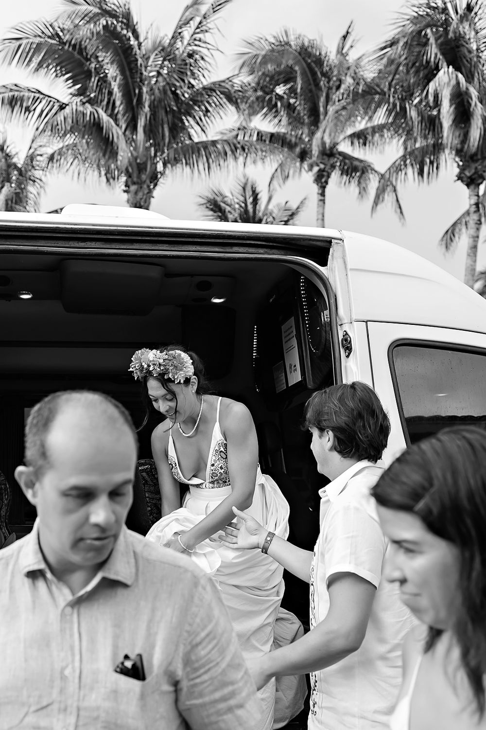 Black and white images of people in white attire getting out of a white minivan near palm trees.