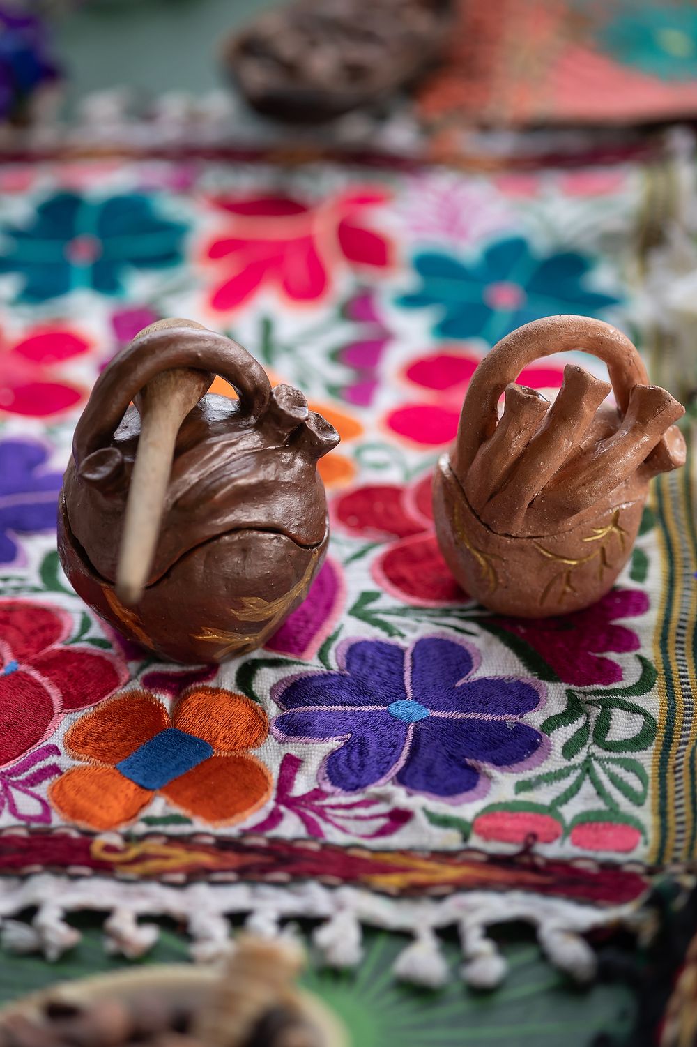 Two chocolate truffles sit on a colorful floral embroidered textile with red, blue and purple flower patterns.