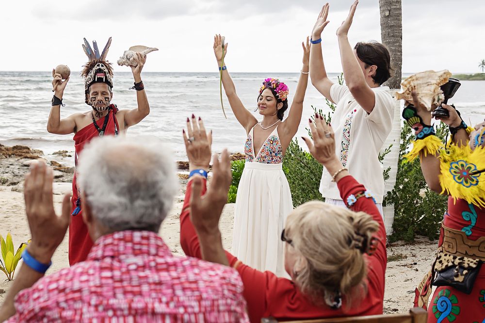 An energetic beach wedding ceremony filled with joy as celebrants raise their hands in celebration by the ocean.