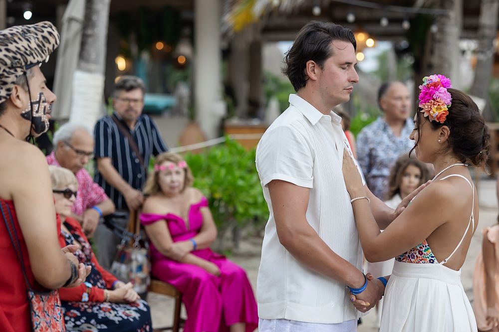 Wedding ceremony guests gather outdoors on a tropical patio with pink floral decor.