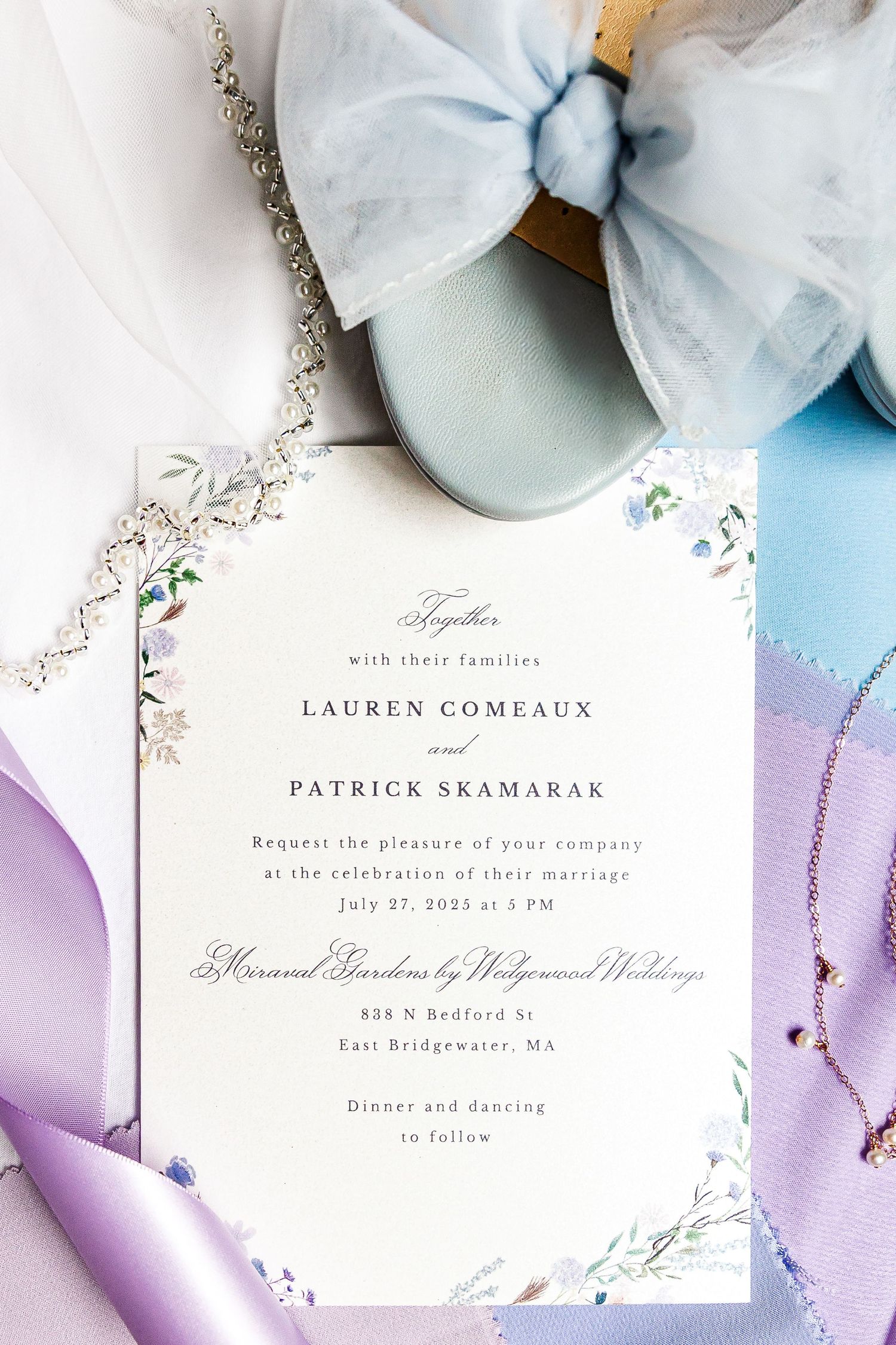 Wedding invitation card with elegant floral design and cursive text on white paper with pastel blue and purple decorative accents.