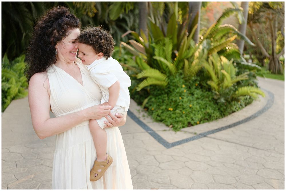 Two people in white wedding attire share an intimate dance moment in a garden setting.