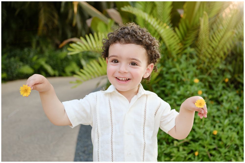 Child in white shirt playing outdoors with flowers in lush garden setting.