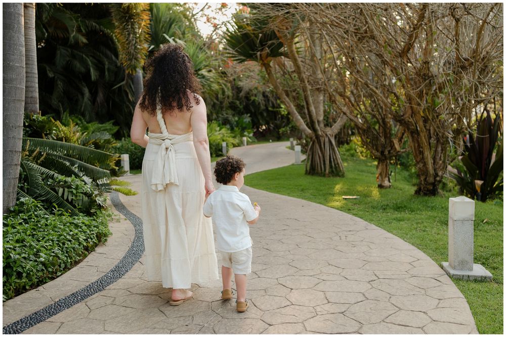 A walkway through a lush garden shows a parent and child walking hand in hand down a stone path.