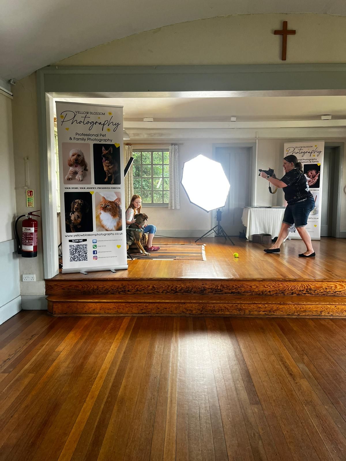 Professional photography studio setup with lighting equipment and display banners in a room with hardwood floors and a cross on the wall.