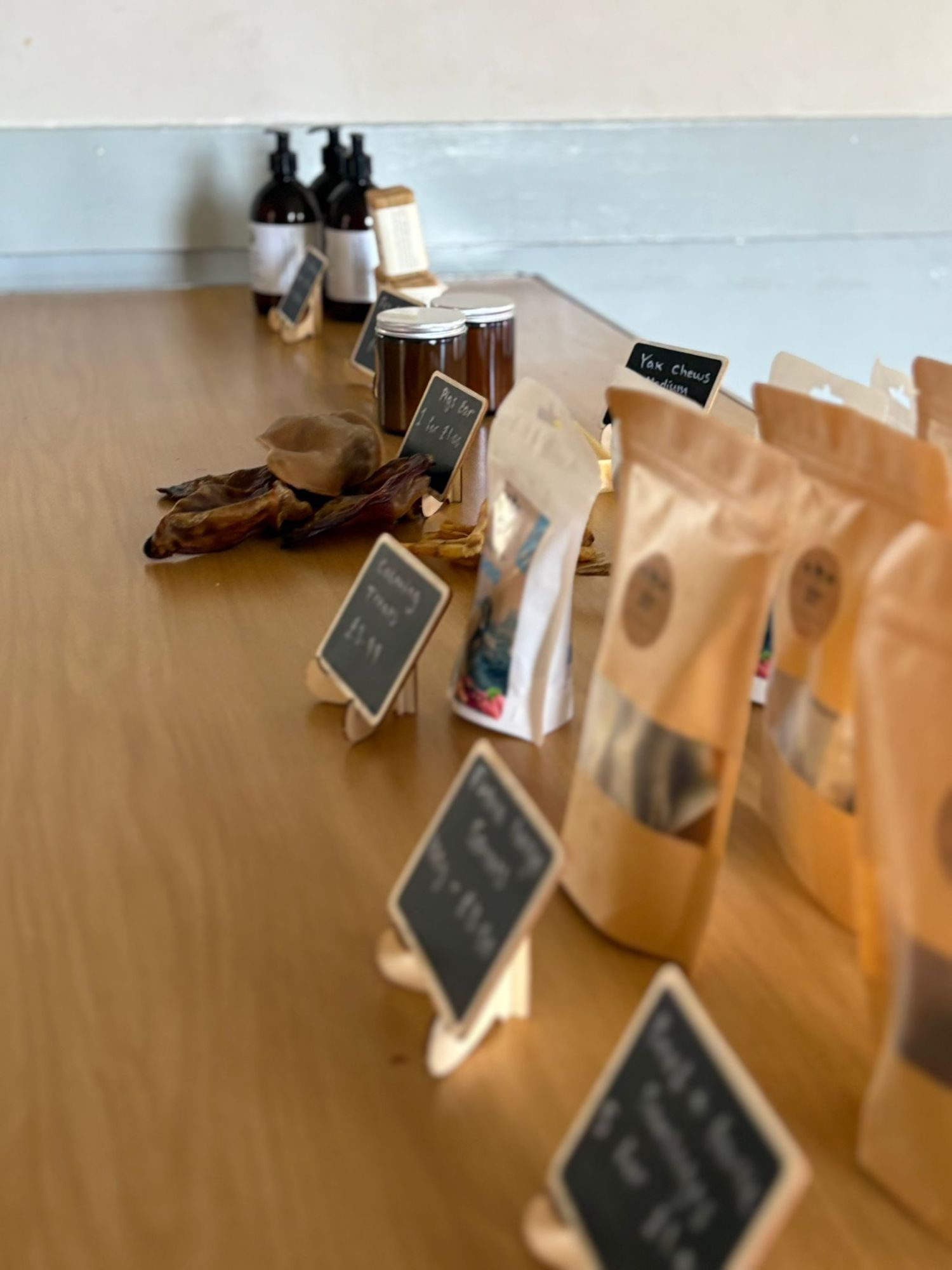 Brown paper bags with small chalkboard labels line up on a wooden table alongside glass bottles and jars.