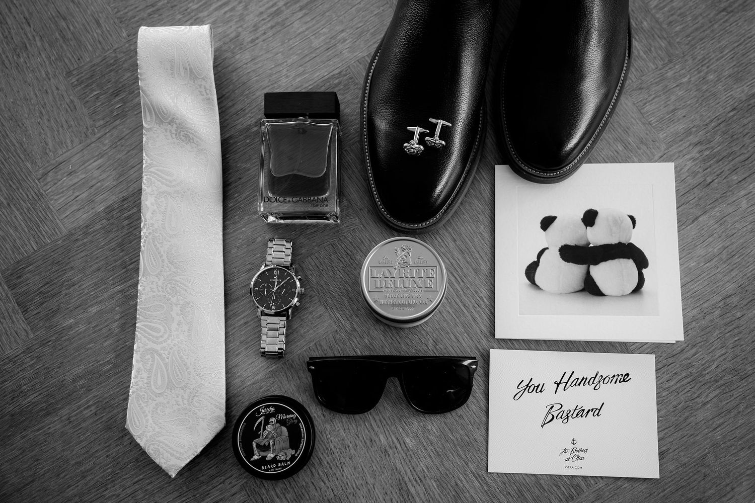 Black and white photograph showing artistic flatlay arrangement of mens fashion accessories and sketches on dark surface.