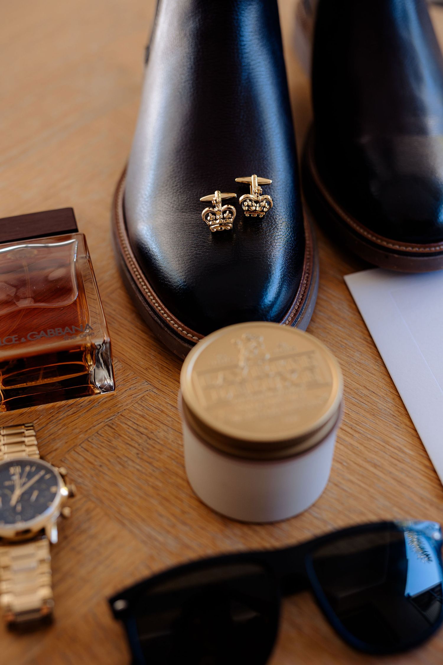 Close-up details of black leather dress shoes with accessories like sunglasses, watch and wallet on wooden surface.