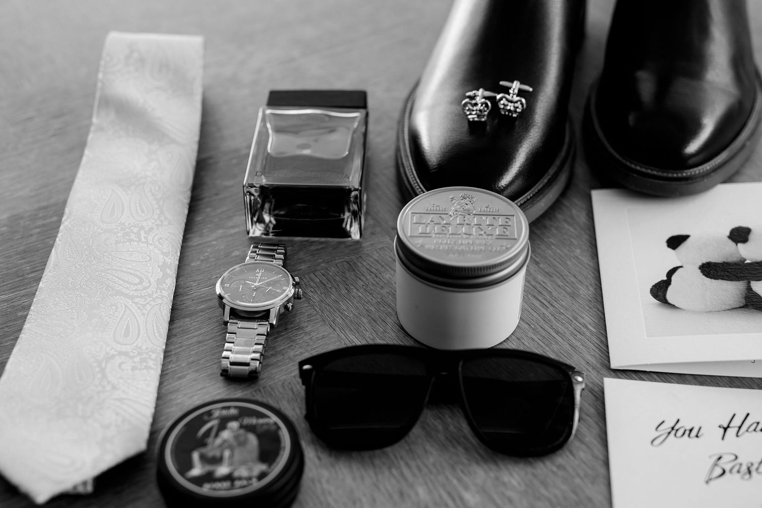 Black and white photo of men's accessories including tie, watch, sunglasses, dress shoes and grooming products.