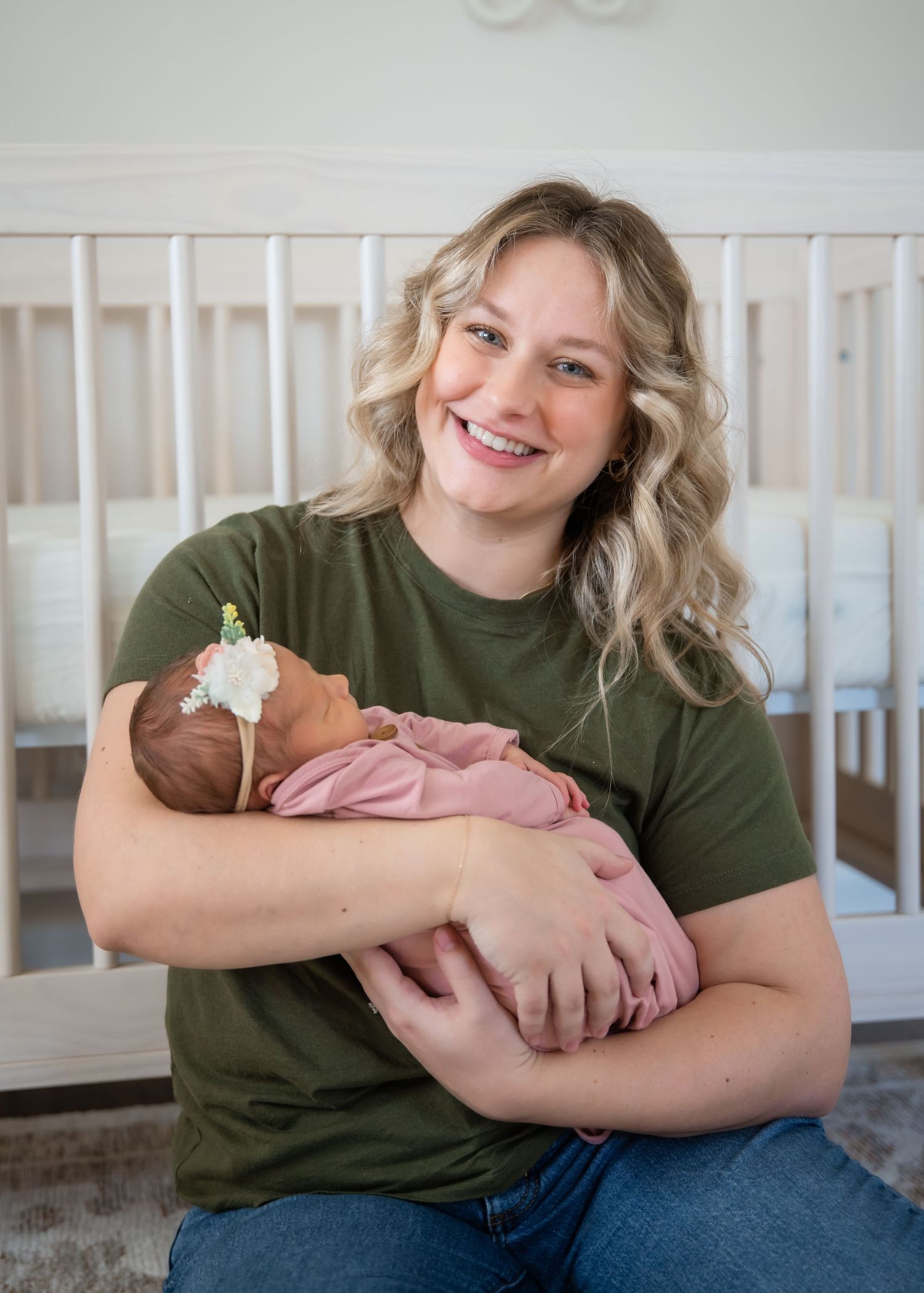 Parent in olive green shirt and jeans cuddles with newborn infant in home nursery setting.