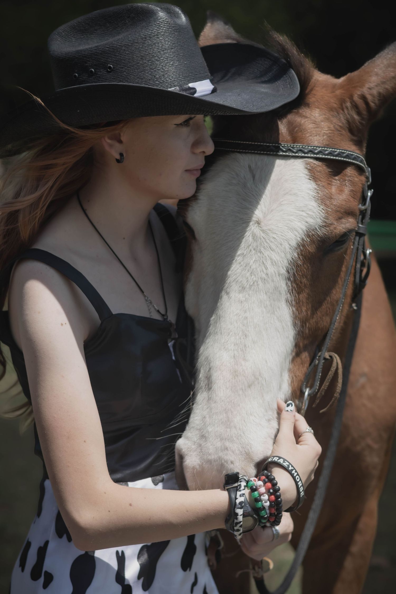 Person wearing a black hat and dark clothing pets a brown and white horse affectionately in multiple close-up shots.