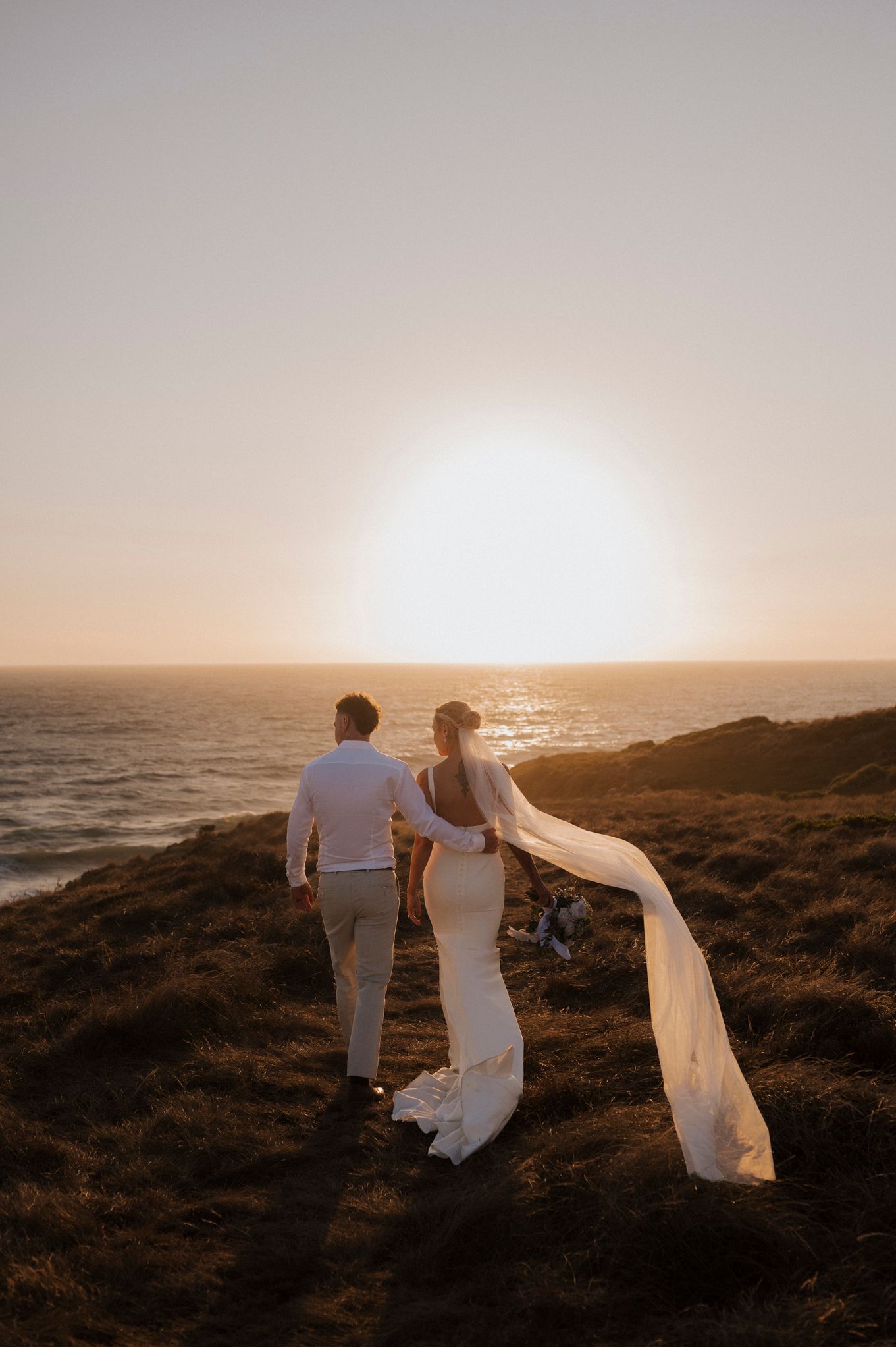 Dramatic sunset wedding photography session on a coastal cliff with flowing veils.