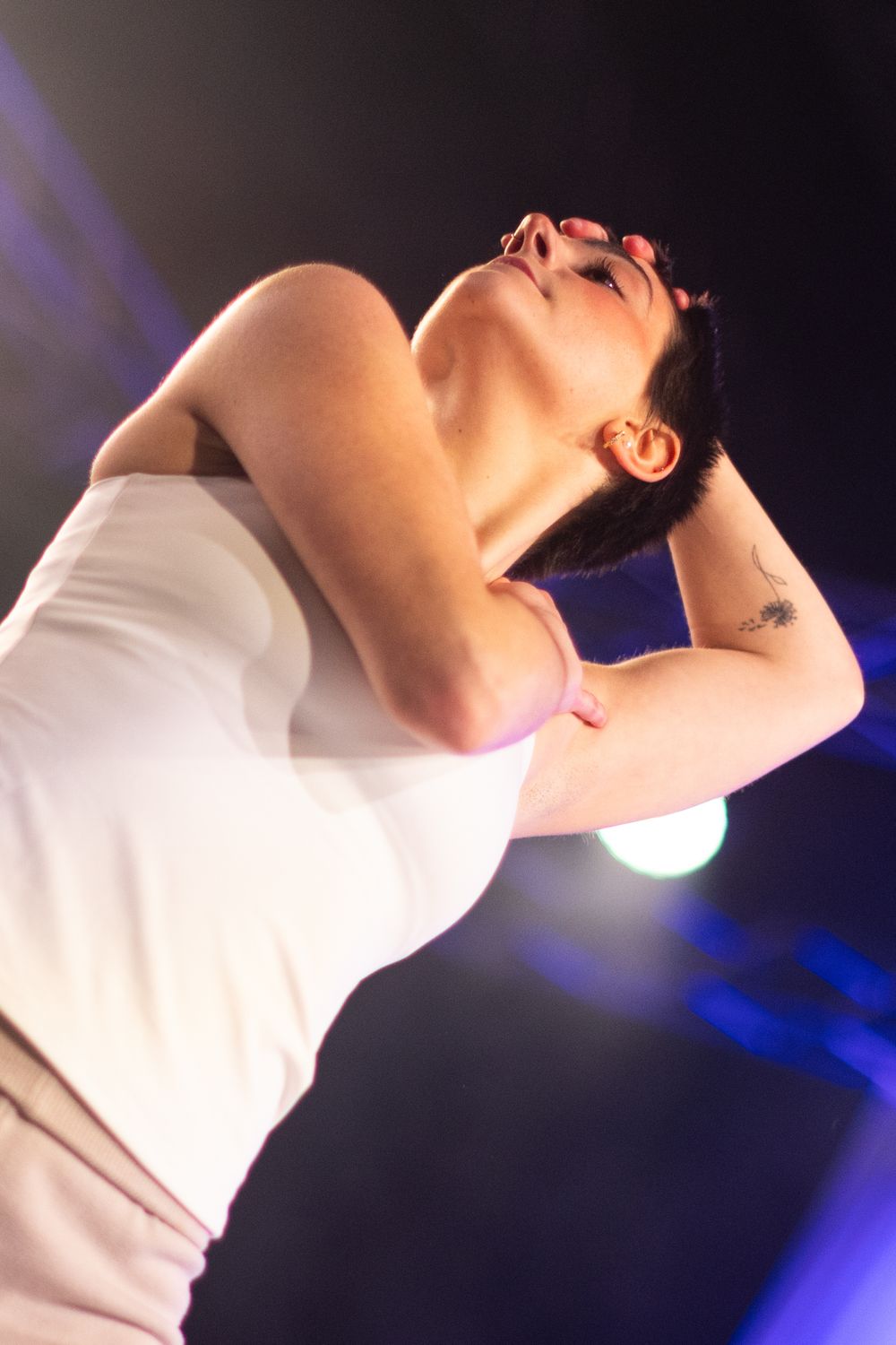 Performer in white shirt arches backwards dramatically against dark stage with blue lighting effects.