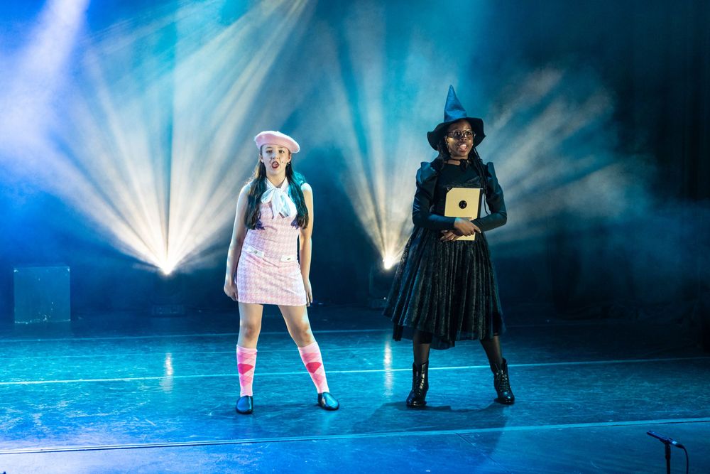 Two performers strike dramatic poses on a stage with dramatic blue lighting and beams creating an ethereal atmosphere.