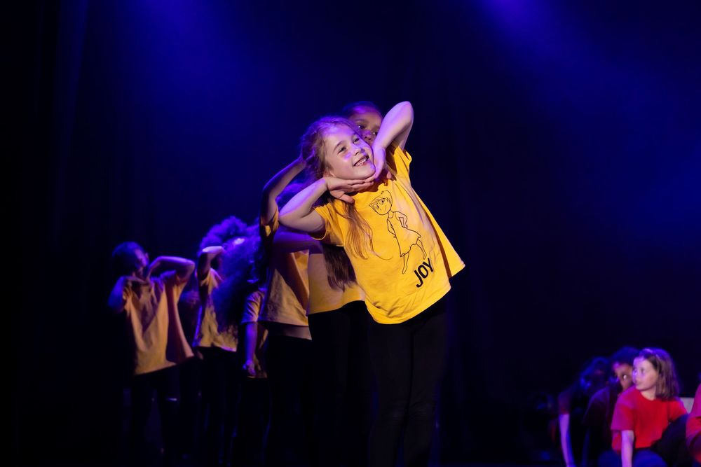 Performers dancing in a dark theater with dramatic blue lighting and shadows.