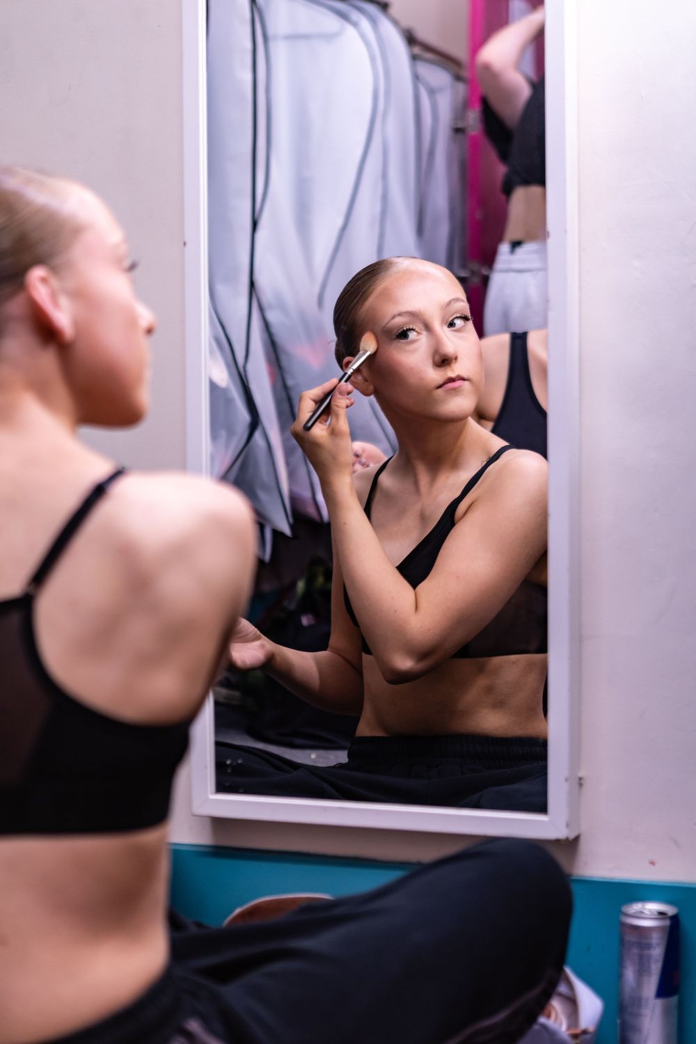 A dancer in a black top applies makeup while looking in a mirror before a performance.
