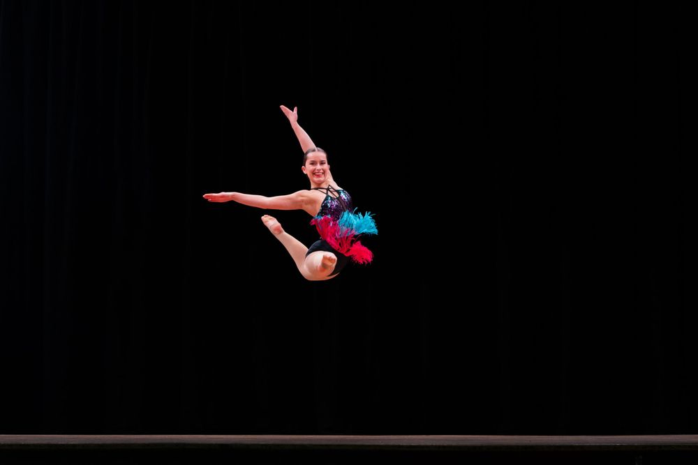 Female gymnast in red leotard performs a graceful split handstand on balance beam during competition.