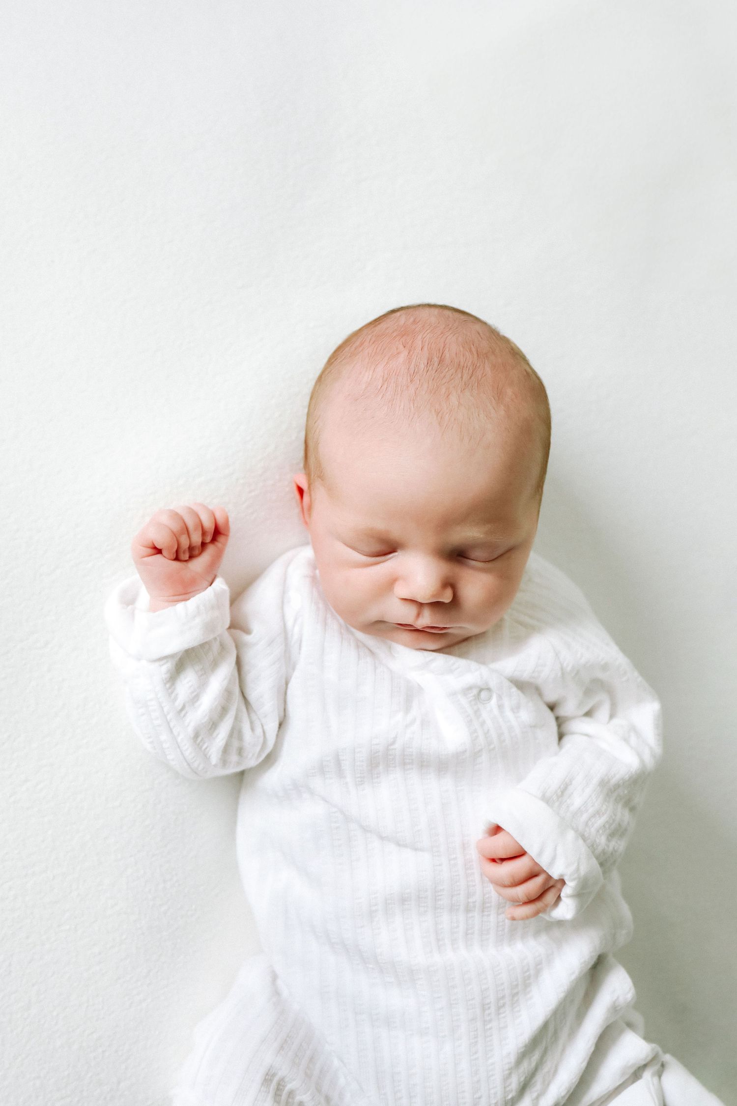 A sleeping baby in white clothing lies on a white surface, creating a serene minimalist composition,during newborn shoot based in Nottingham
