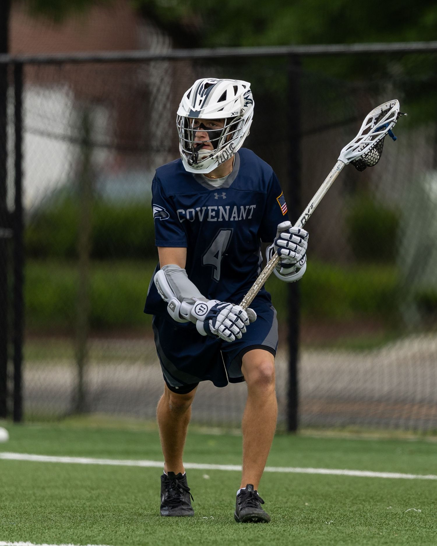 Lacrosse player in white uniform reaches for ball during field game.
