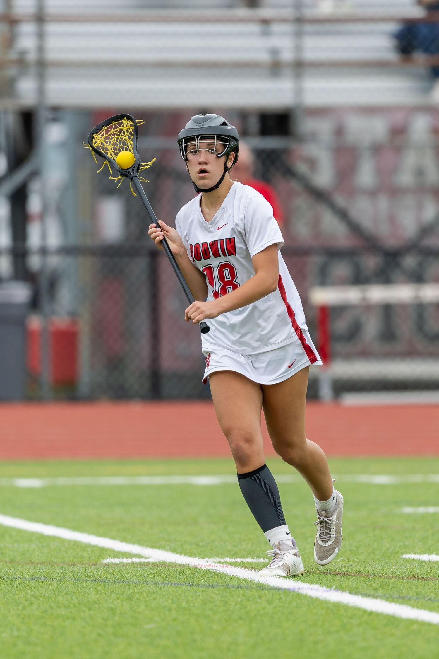 Lacrosse player in white uniform reaches for ball during field game.
