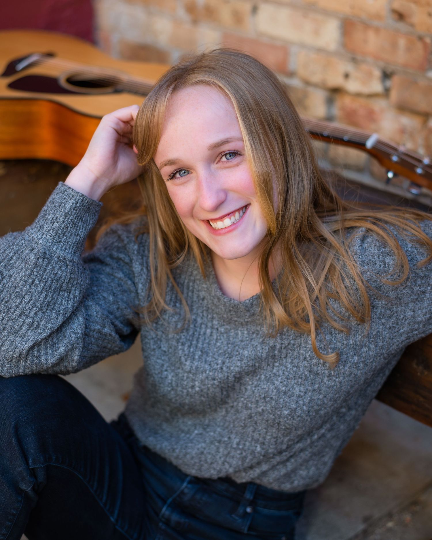 A series of warm portraits showing someone in a cozy gray sweater sitting against a rustic brick wall.