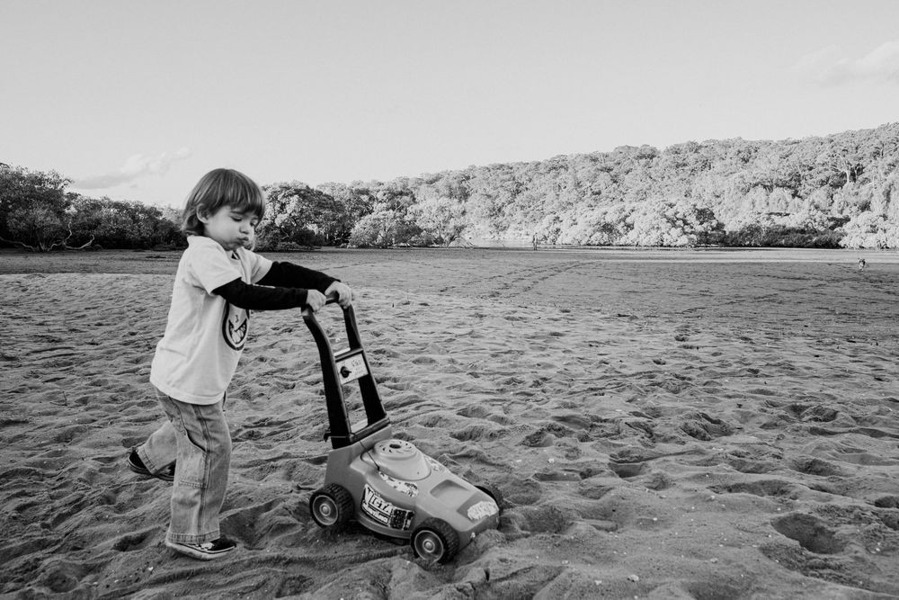 Child playing with toy truck on sandy beach in black and white photograph.