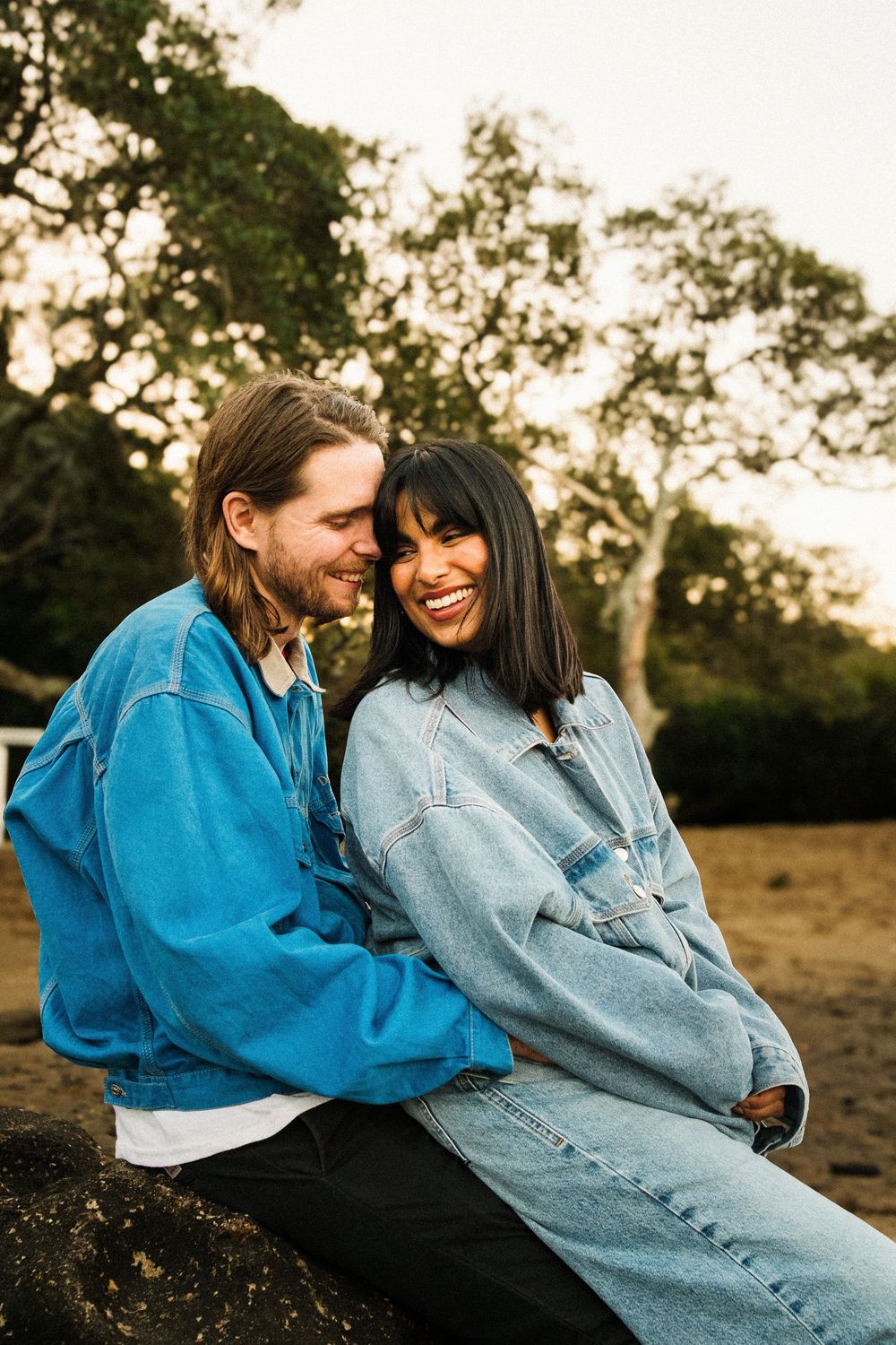 Couple in denim and blue jackets sharing a joyful moment outdoors at sunset.